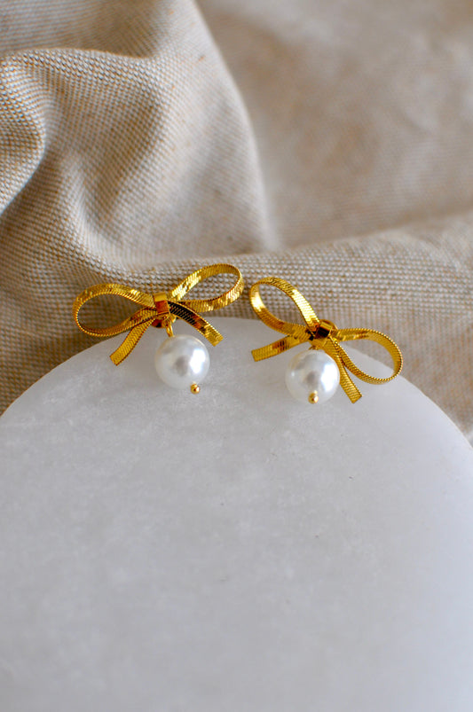 Gold bow earrings with pearls on a marble surface and fabric background