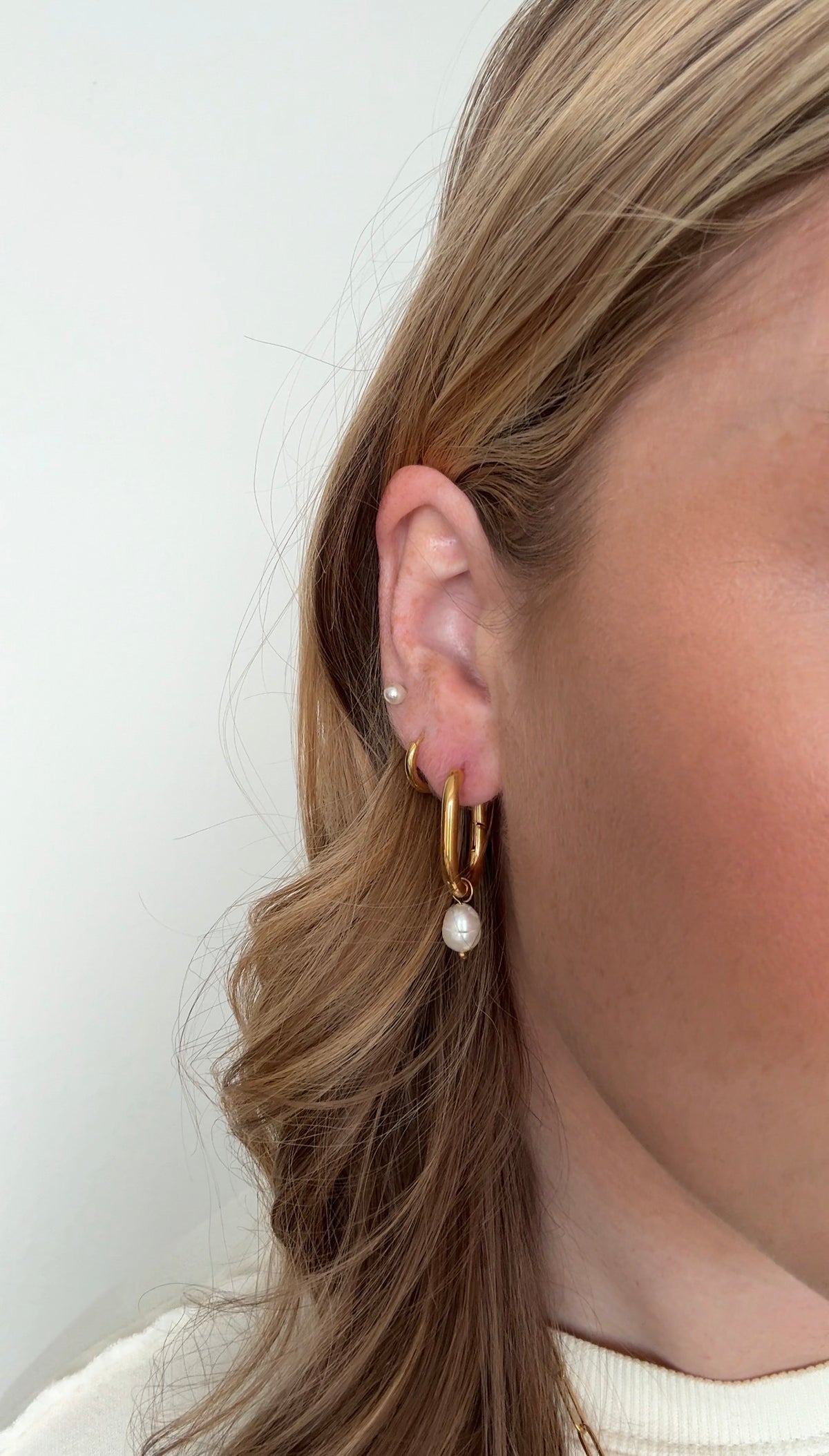 Close-up of a person wearing gold earrings with pearls against a white background