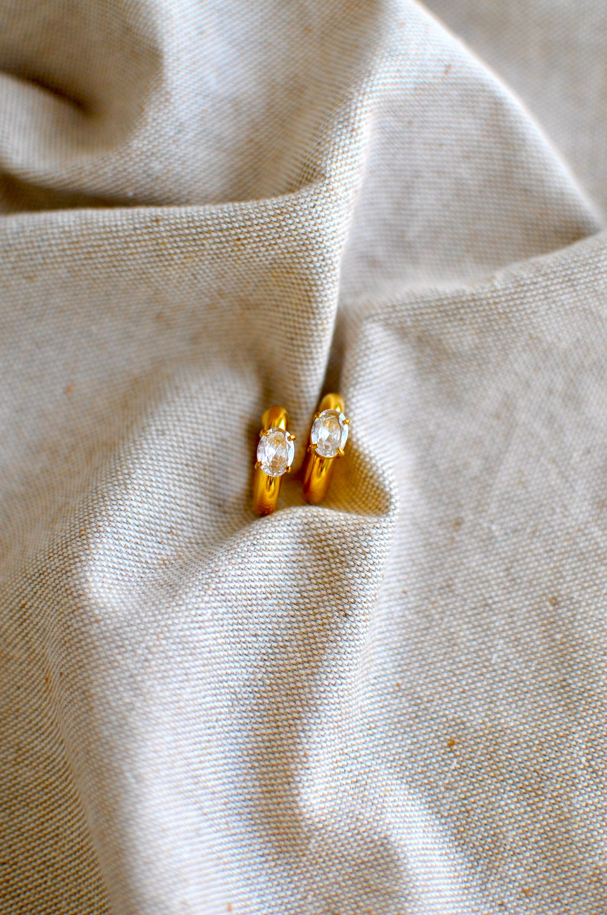 Pair of gold earrings with gemstones on a beige fabric background
