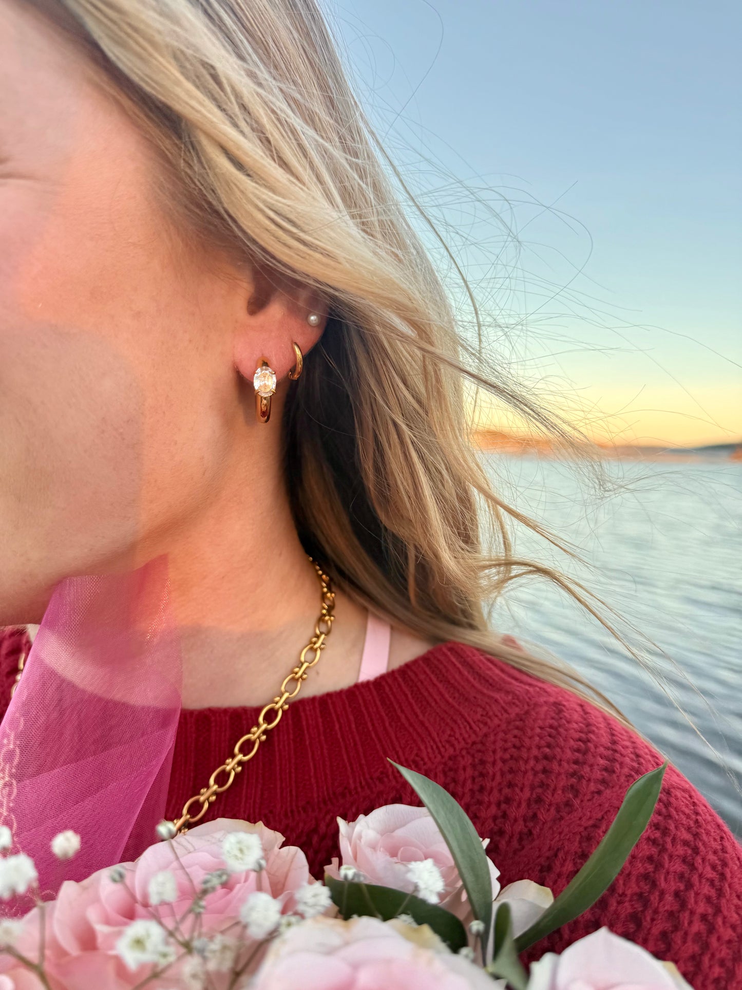 Woman wearing gold earrings with a sunset over water in the background