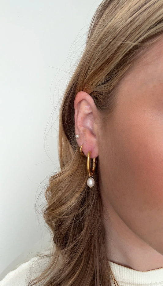 Close-up of a person wearing gold earrings with pearls against a white background